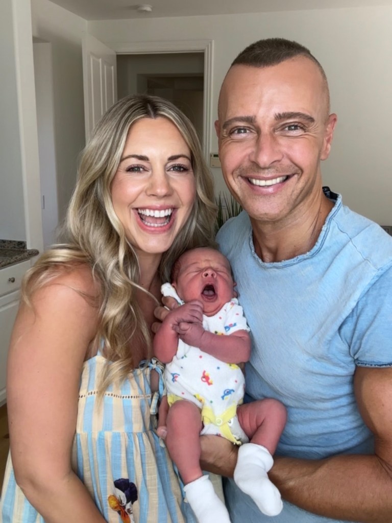 A smiling man and woman holding a newborn baby who is yawning.