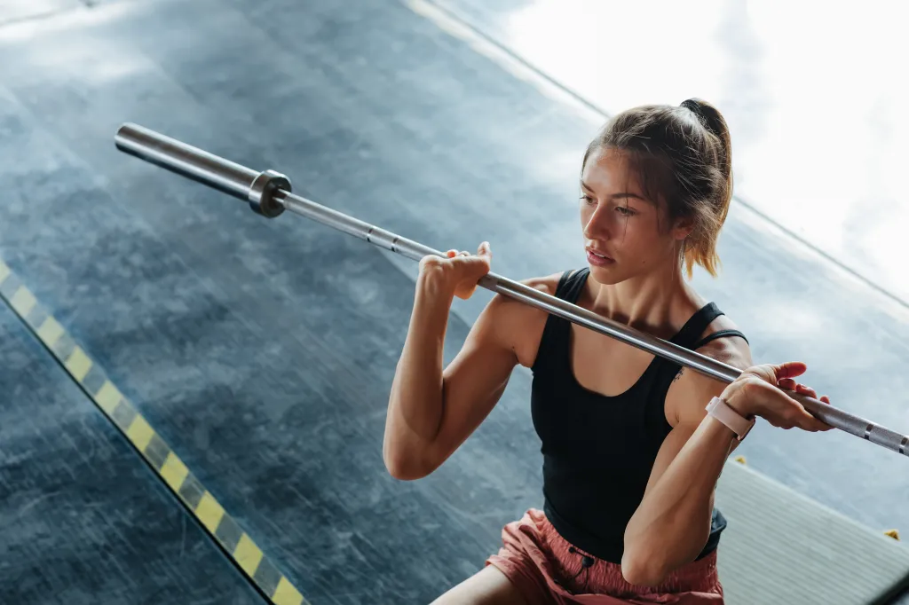 A young woman in a black tank top and pink shorts lifts a barbell.
