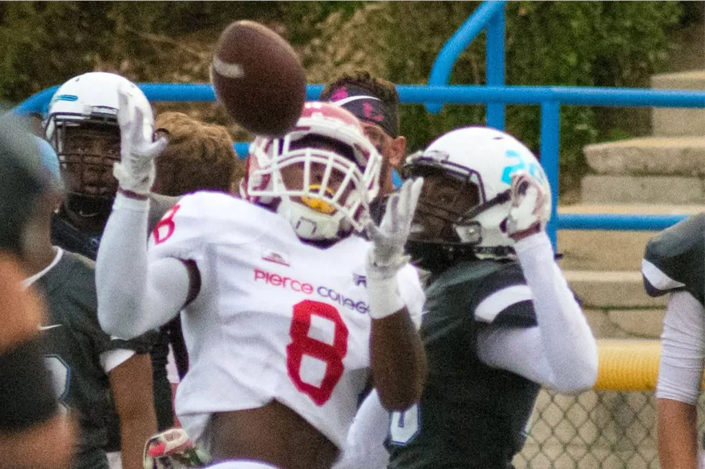 Two football players in helmets reaching for a football in mid-air.