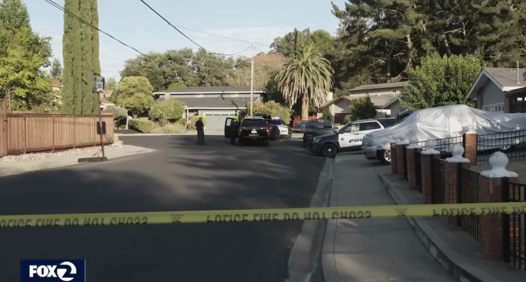 Police cars and officers gathered in a residential street behind yellow caution tape.