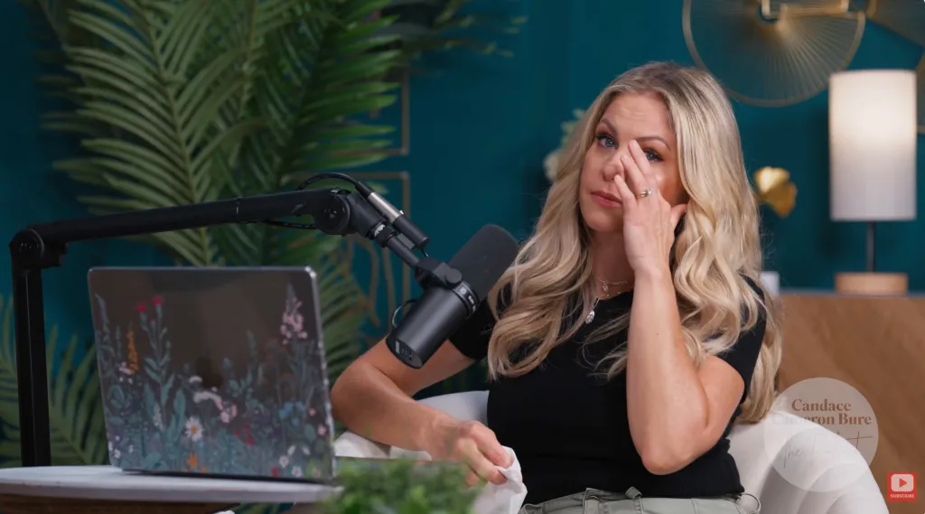 Woman with blonde hair wiping tears from her eyes, sitting next to a microphone and a laptop.