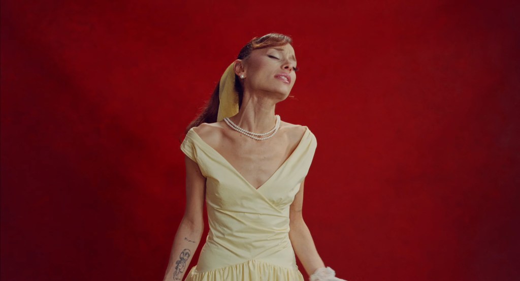 Ariana Grande in a yellow dress with pearls against a red background.