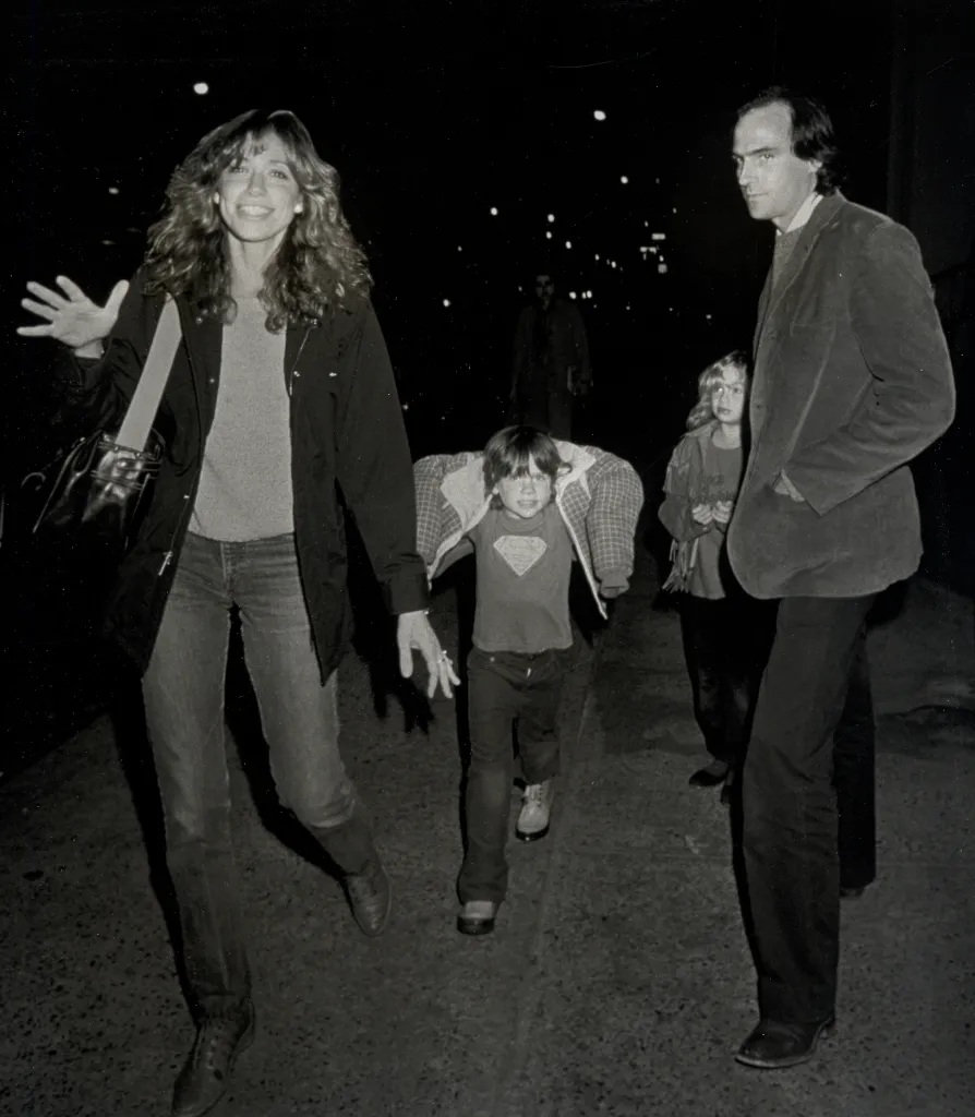 James Taylor playing guitar and singing next to Carly Simon singing into a microphone.
