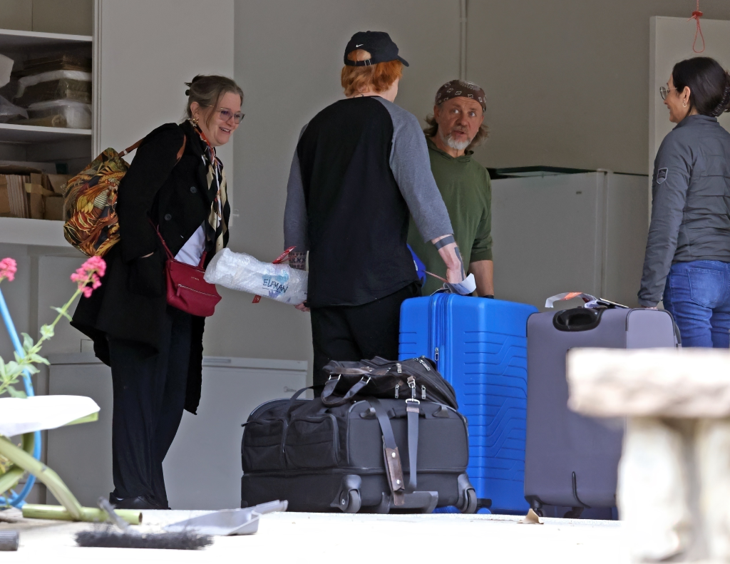 Bridget Fonda and Danny Elfman with suitcases talking to a contractor.