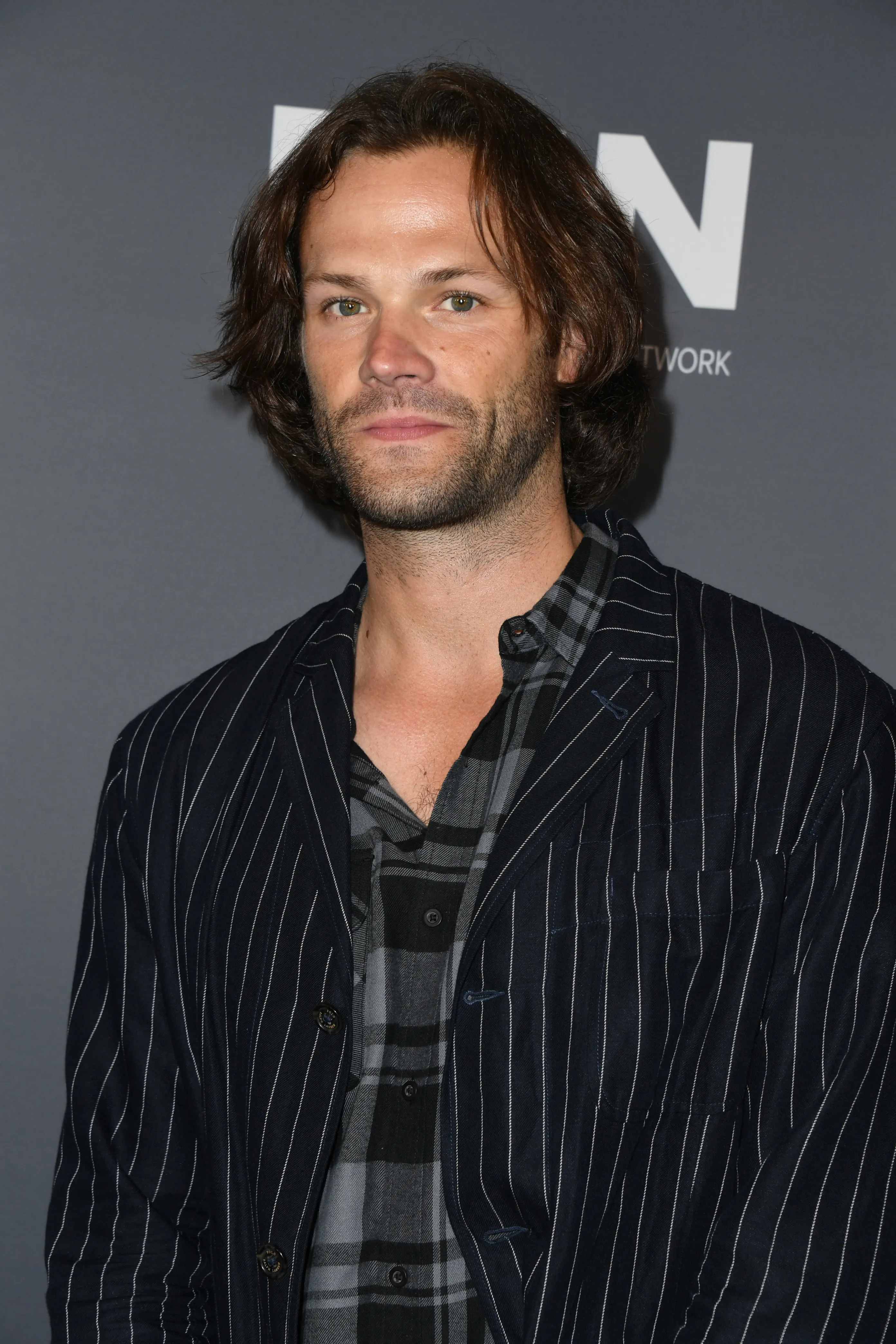 Jared Padalecki in a pinstriped jacket over a plaid shirt.