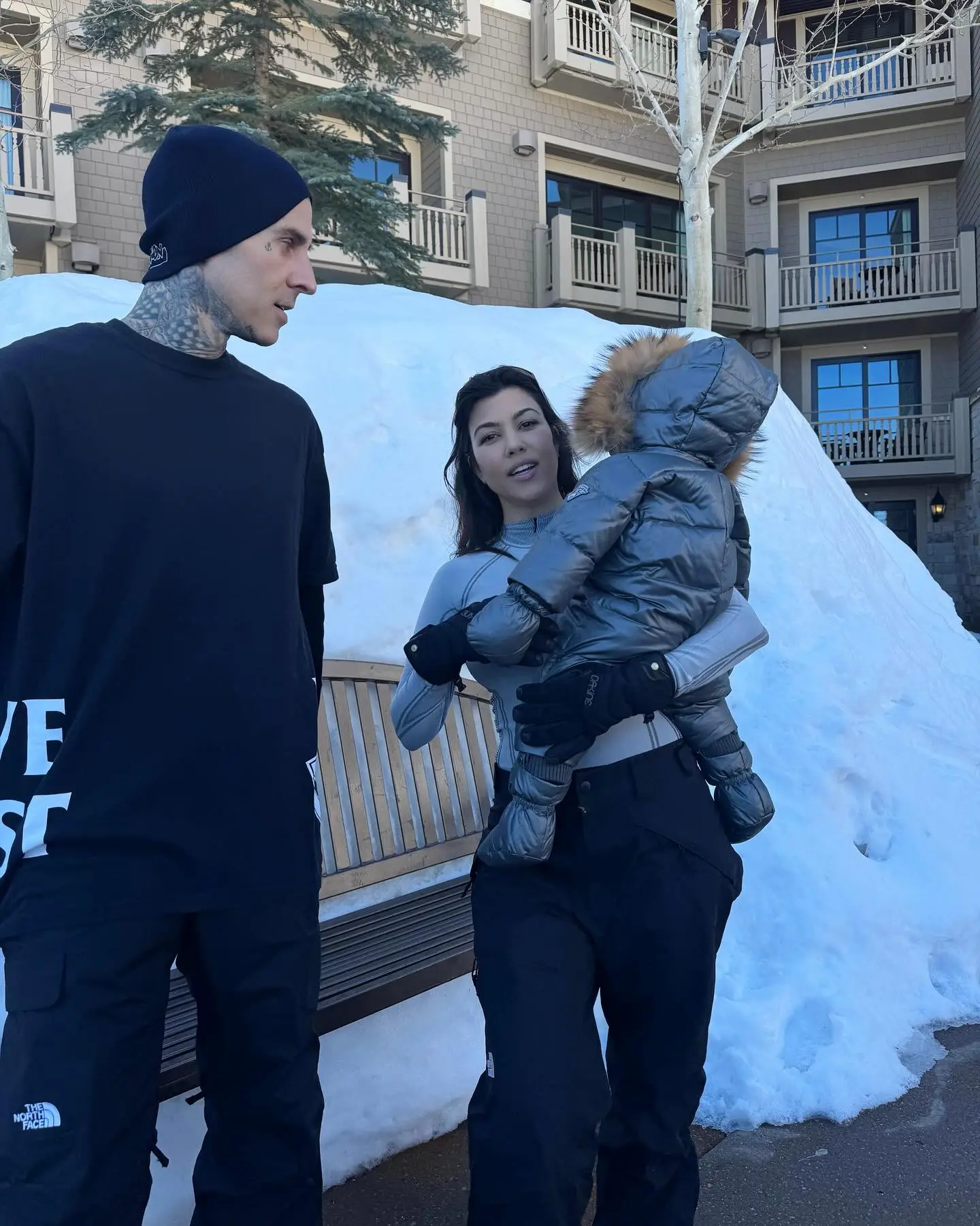 Kourtney Kardashian holding Roxky, with Travis Barker beside them, in a snowy outdoor setting.