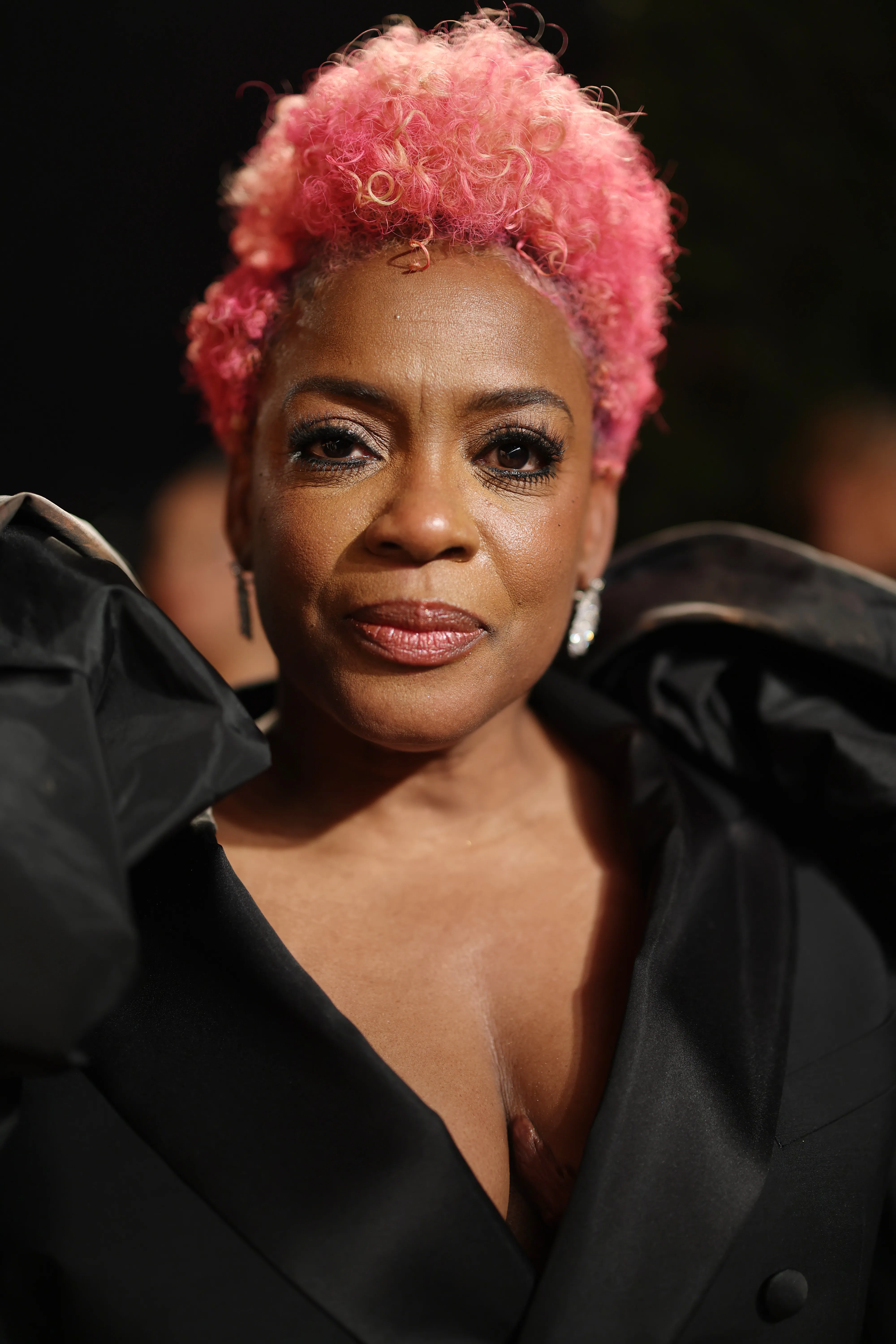 Aunjanue Ellis-Taylor with pink curly hair, wearing a black satin jacket and diamond earrings, attending the 2025 Vanity Fair Oscar Party.