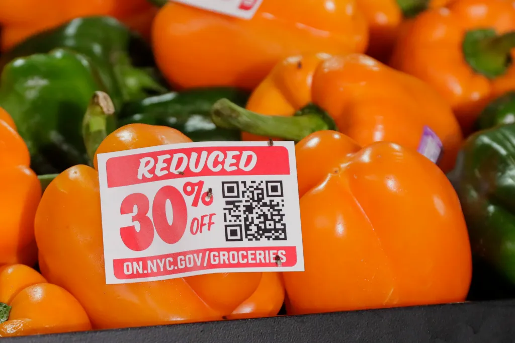 A "Reduced 30% Off" sticker on an orange bell pepper, with a QR code and website address, surrounded by other orange and green bell peppers.