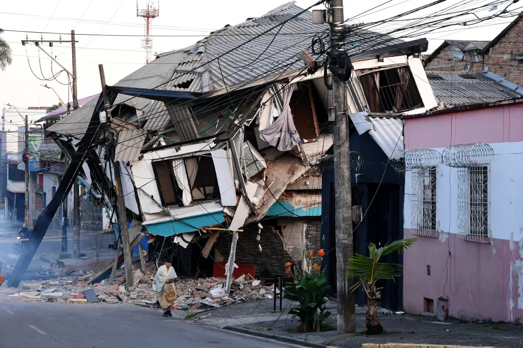 A collapsed house in Pereira, Colombia, after an earthquake, with a person walking on the street.