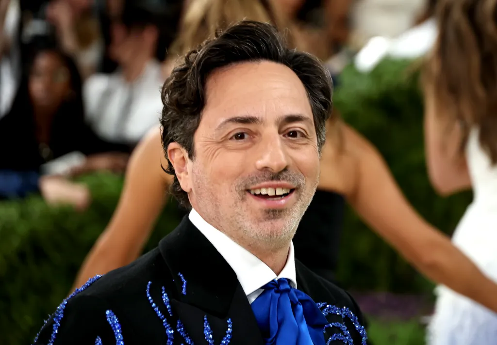 Sergey Brin smiling at the 2026 Met Gala, wearing a black suit with blue embellishments and a blue bow tie.