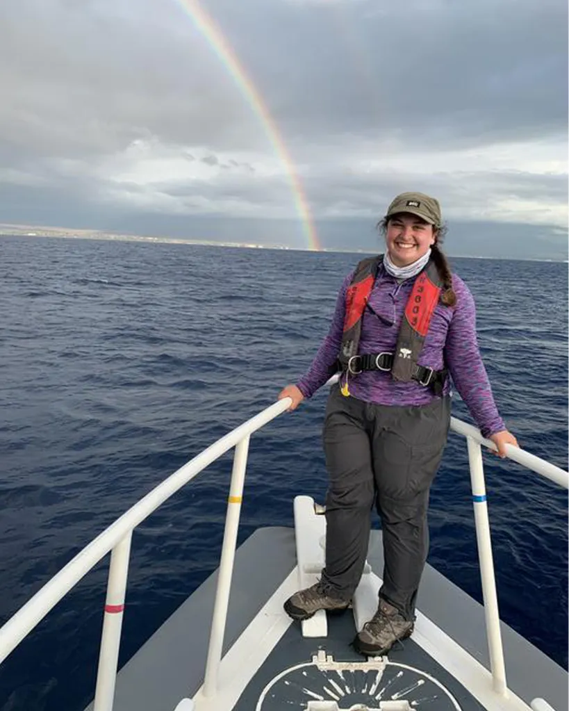 Dr. Julia Zeh smiling on a boat with a rainbow in the sky.