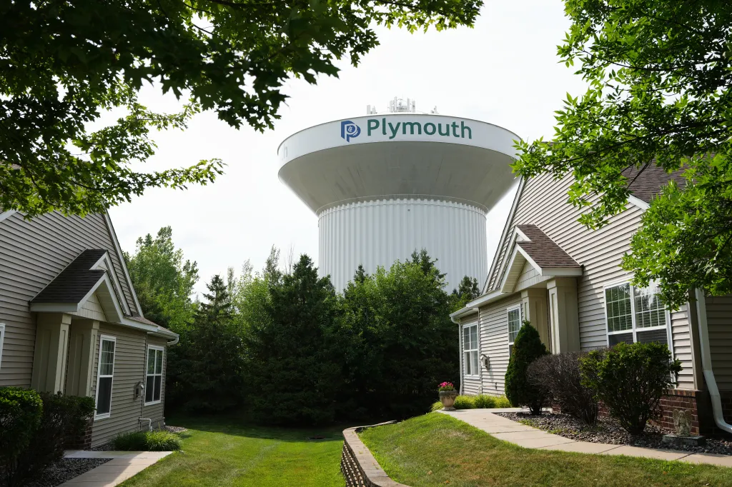 A water tower with "Plymouth" written on it rises above houses and trees.