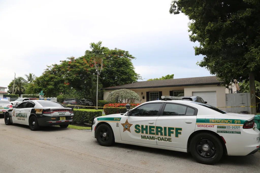 Two Miami-Dade Sheriff's cars are parked on a residential street with caution tape across a yard in Westchester, Florida.