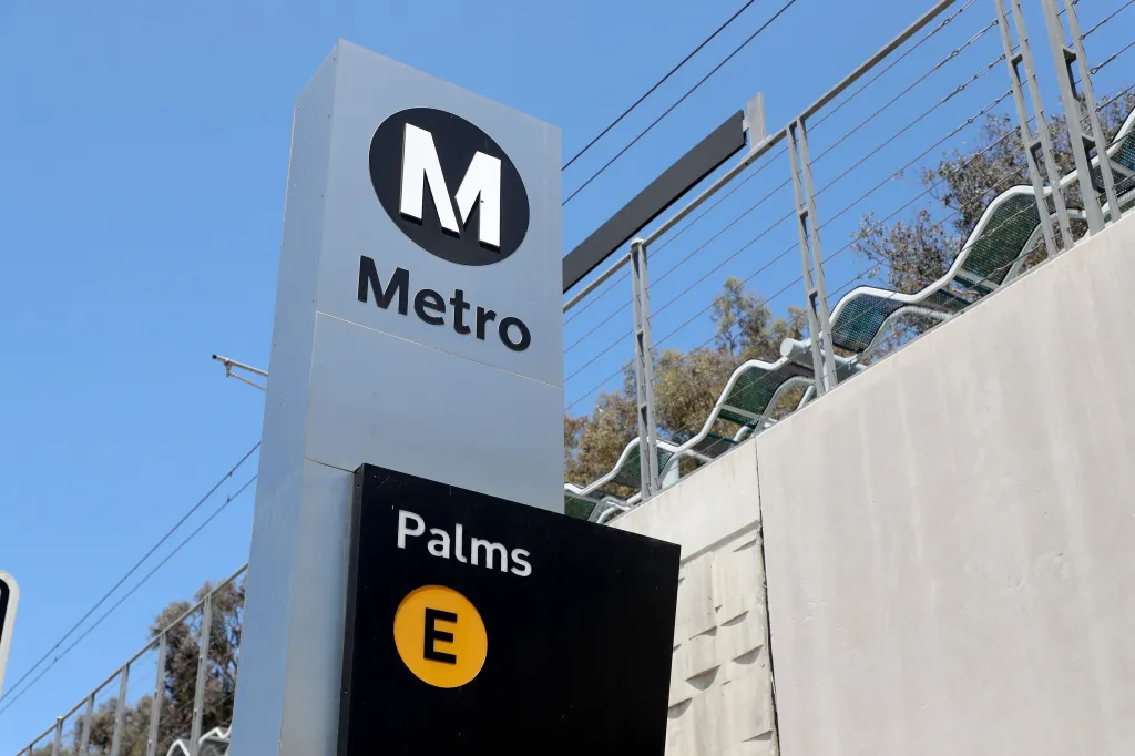 A Metro sign with a large "M" logo and the word "Metro" above a black sign that says "Palms E."