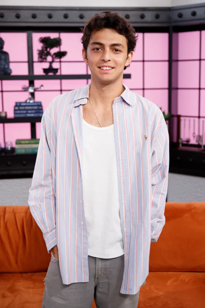 Shai Fruchter smiles in a striped button-up shirt over a white tank top and gray jeans.