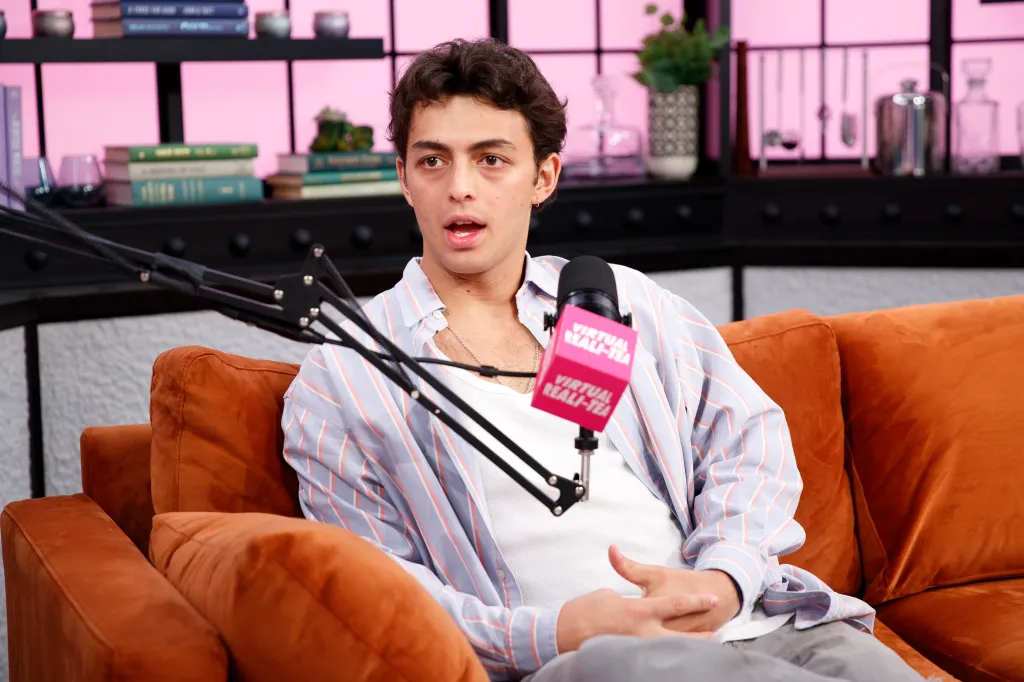 Shai Fruchter speaking into a "Virtual Reali-Tea" microphone while sitting on an orange couch.
