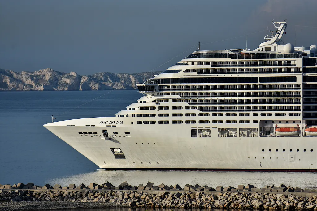 The cruise ship MSC Divina passing by a rocky coastline.
