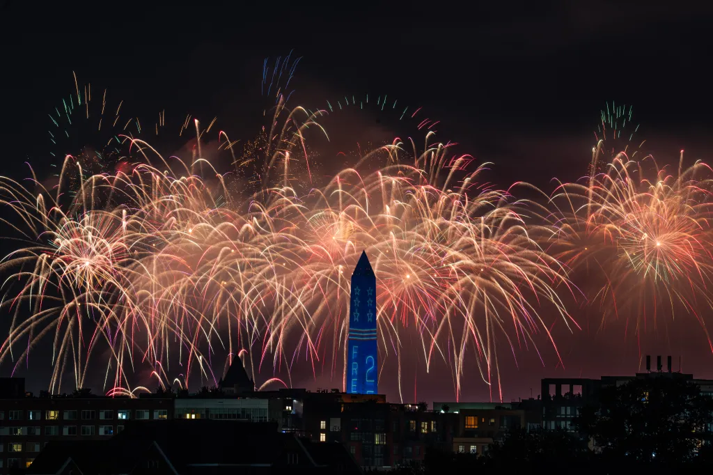 Fireworks bursting over a cityscape with a blue monument lit with stars and the text "FREE 2" on it.