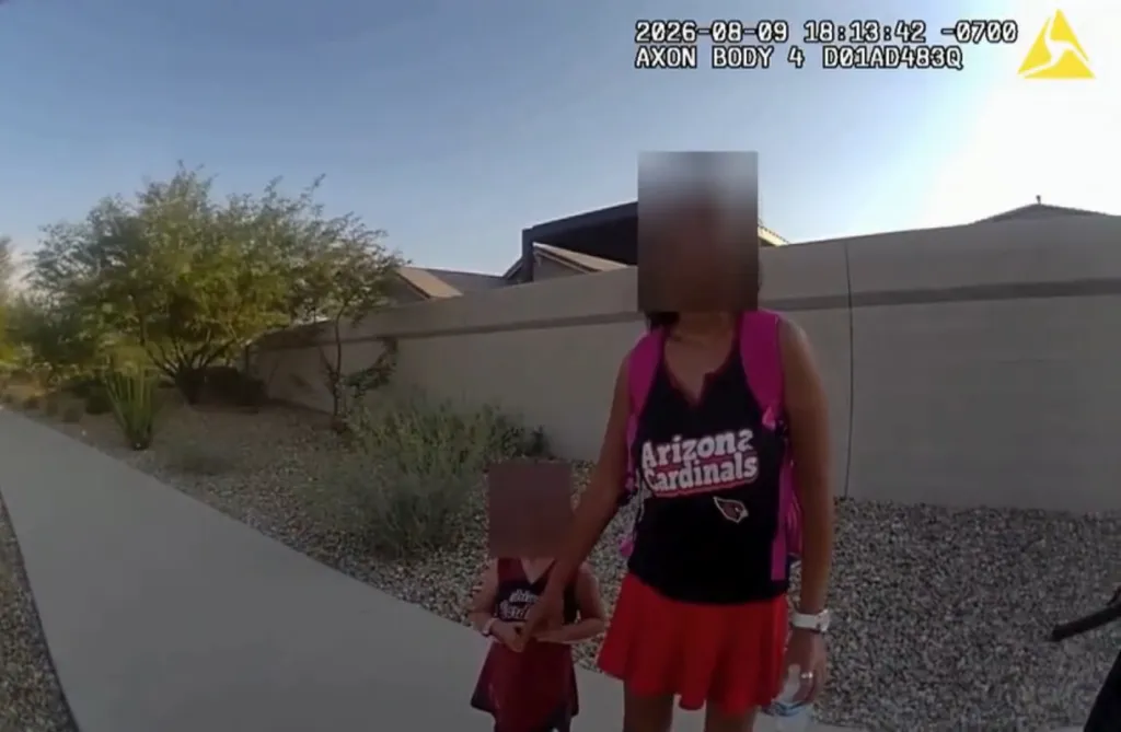 A bodycam still of a woman and child, both wearing Arizona Cardinals apparel, with their faces blurred, standing on a sidewalk.