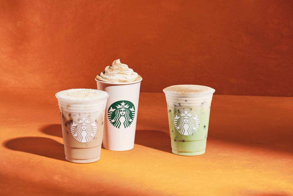 Three Starbucks drinks, including a hot drink with whipped cream and two iced drinks, against an orange background.