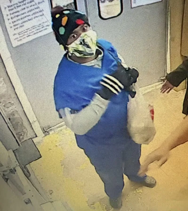 Tracy Daryl Mingo wearing a blue shirt, black hat, and face mask, reaching for something in the bottom right corner.