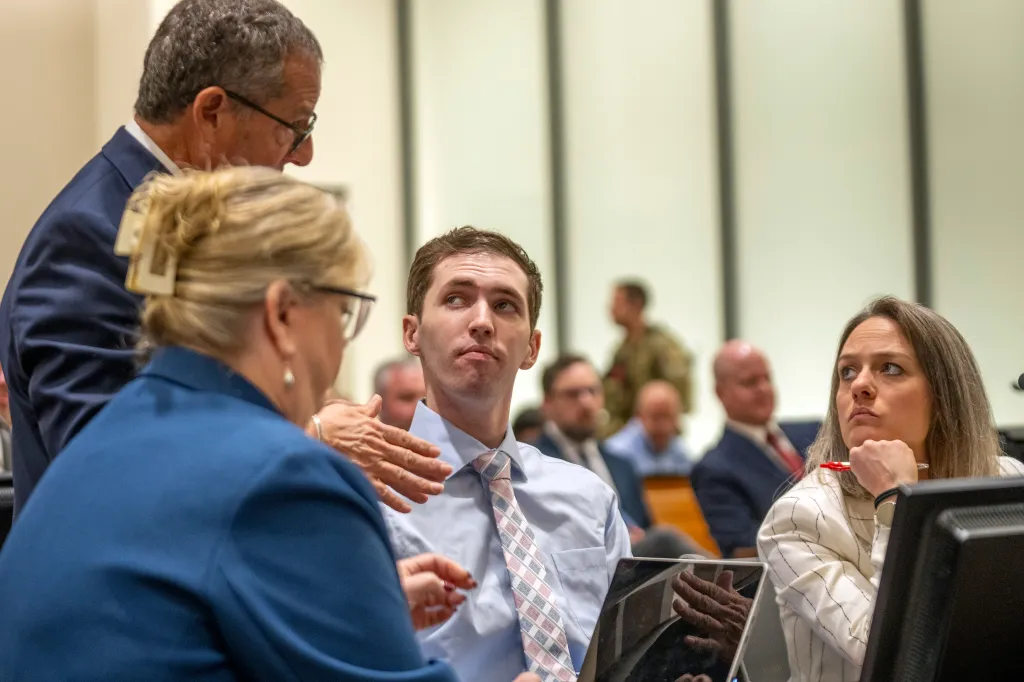 Tyler Robinson (center) looks up while speaking with his attorneys Richard Novak (top left), Kathryn Nester (bottom left), and Staci Visser (right) at a court hearing.
