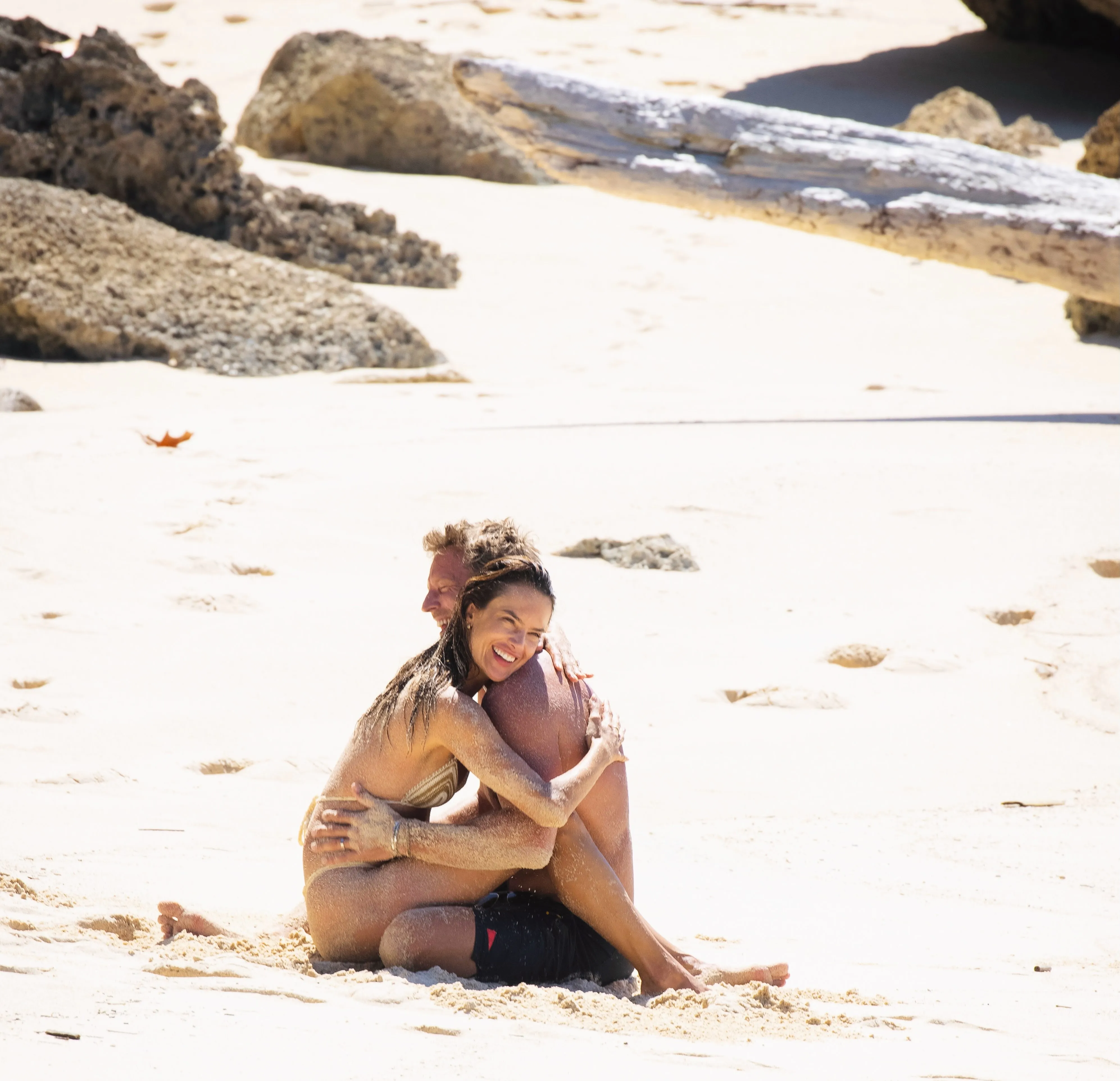 Alessandra Ambrosio and Buck Palmer embracing on a sandy beach.