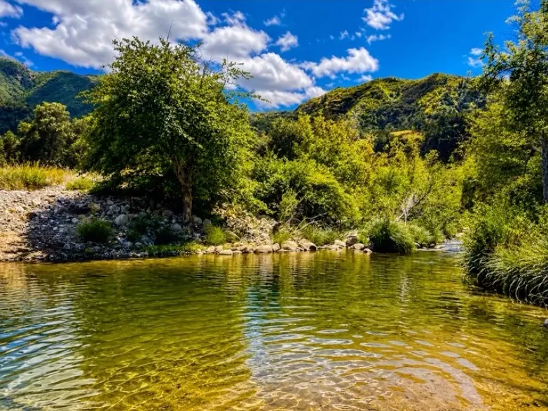 Arroyo Seco, California, with clear water and green hillsides under a blue sky.