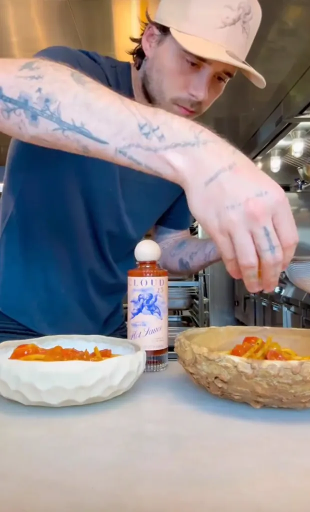 A man sprinkles garnish on two plates of food, with a bottle of hot sauce between them.