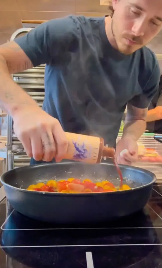 Man pouring liquid from a bottle into a pan of cooking vegetables.