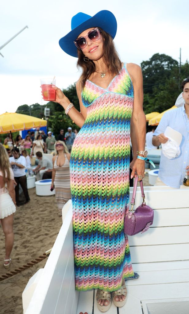 Bethenny Frankel in a pink lace dress talking to a man in a white shirt and pink "supermodel" hat at her Supermodel Cafe pop-up.