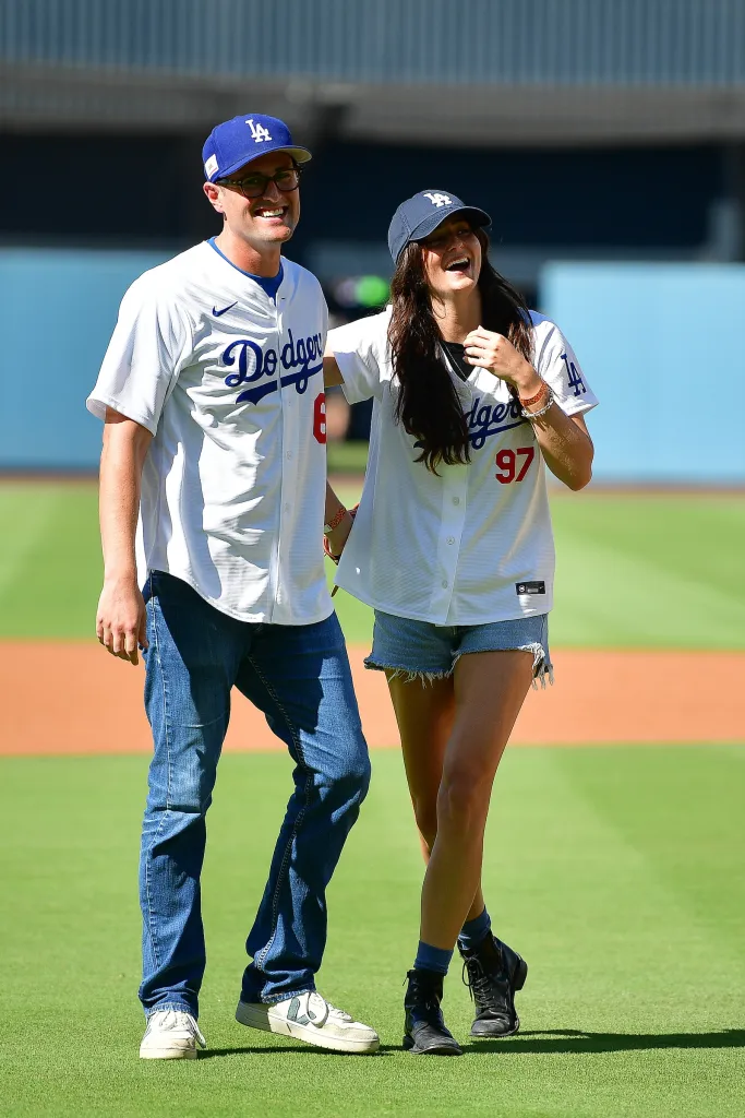 A man and a woman in Los Angeles Dodgers jerseys laugh on the field.