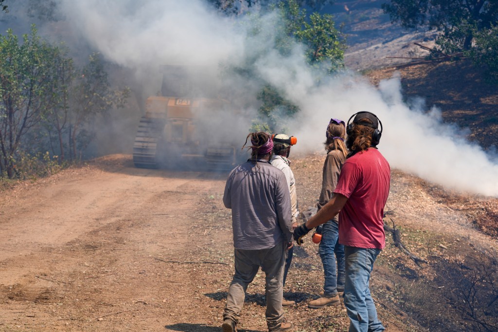 Bulldozer creating firebreak during the "Timber Fire" wildfire in Big Sur, California, with firefighters standing nearby.