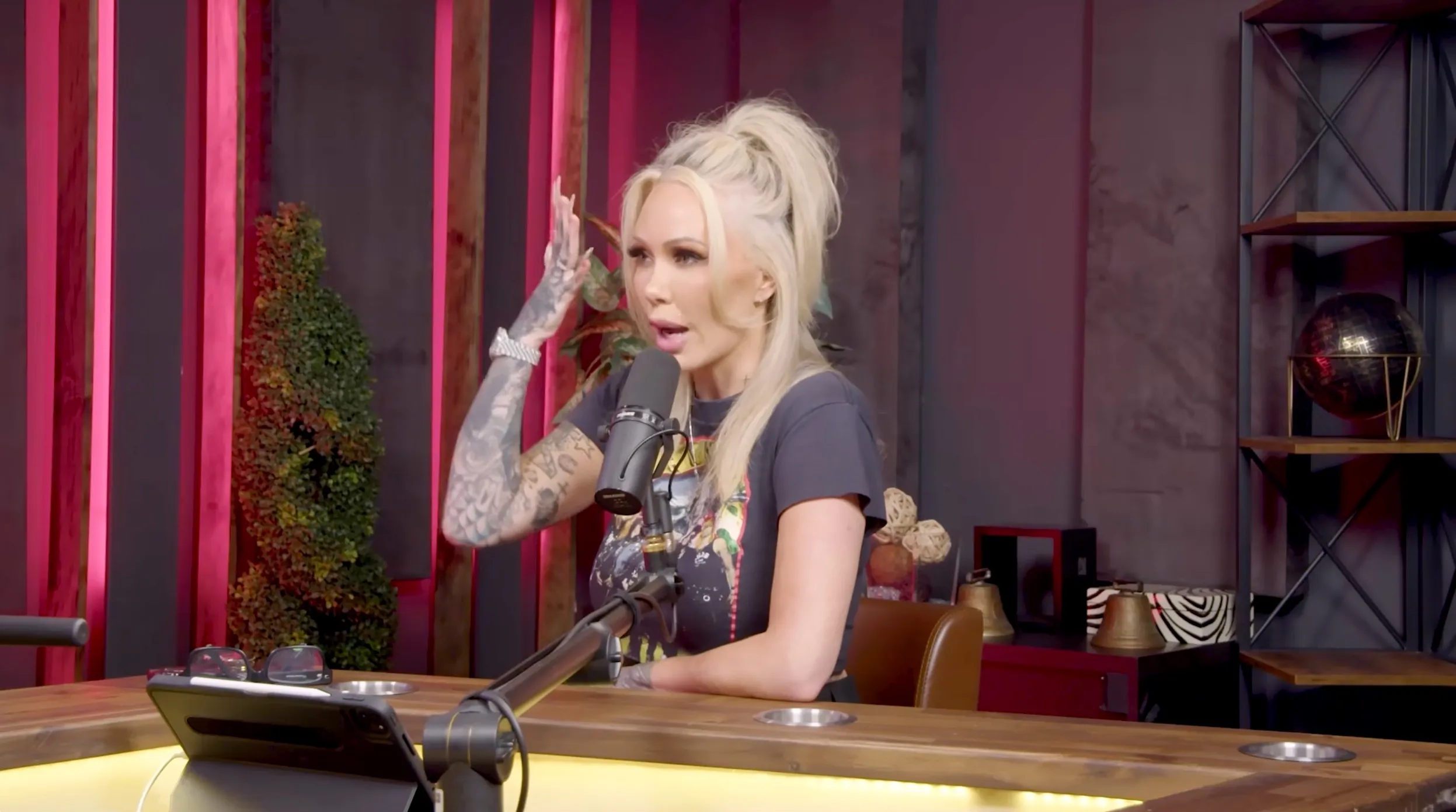 Bunnie Xo speaking into a microphone, gesturing with a tattooed arm.