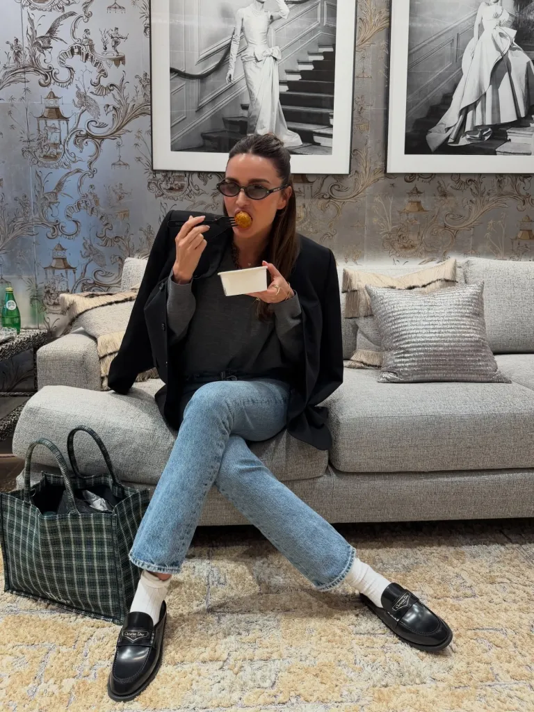 Miranda Kerr eating from a small white container while sitting on a gray couch.