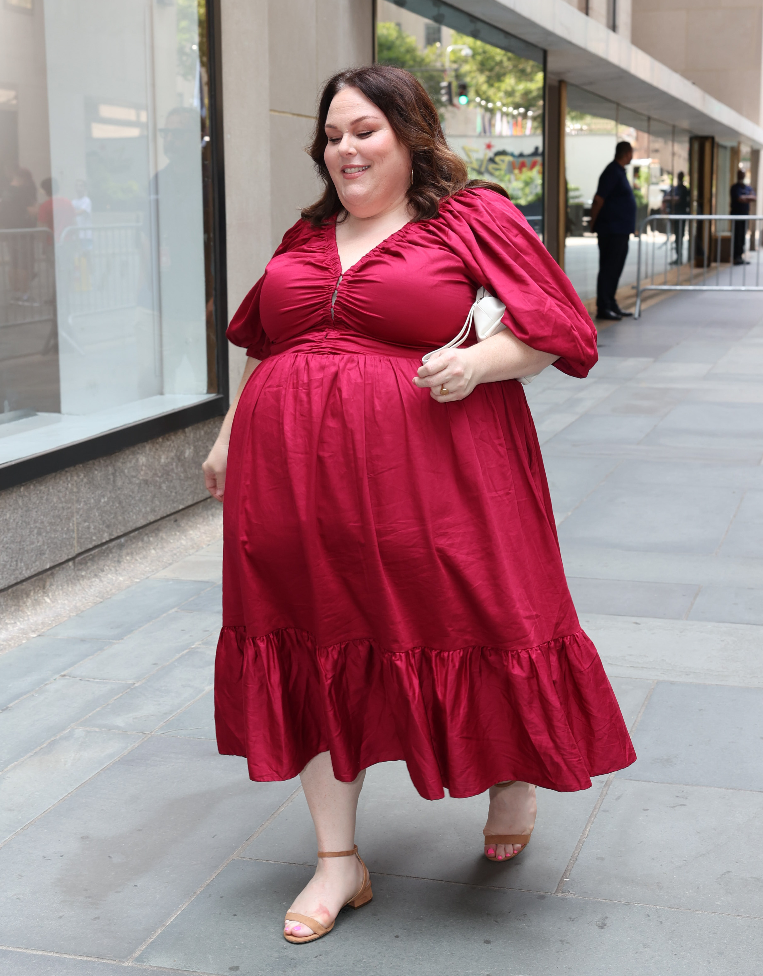 Chrissy Metz in a red dress smiling on a city sidewalk.