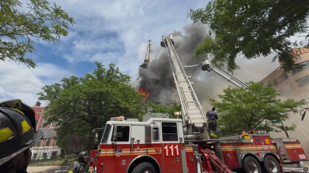 Firefighters on ladder trucks combat a large fire and smoke billowing from a church.