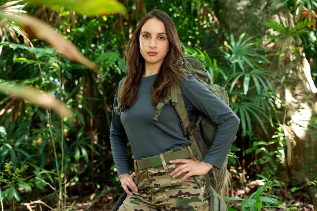Alexia Umansky in military-style gear and a backpack, standing in a jungle.