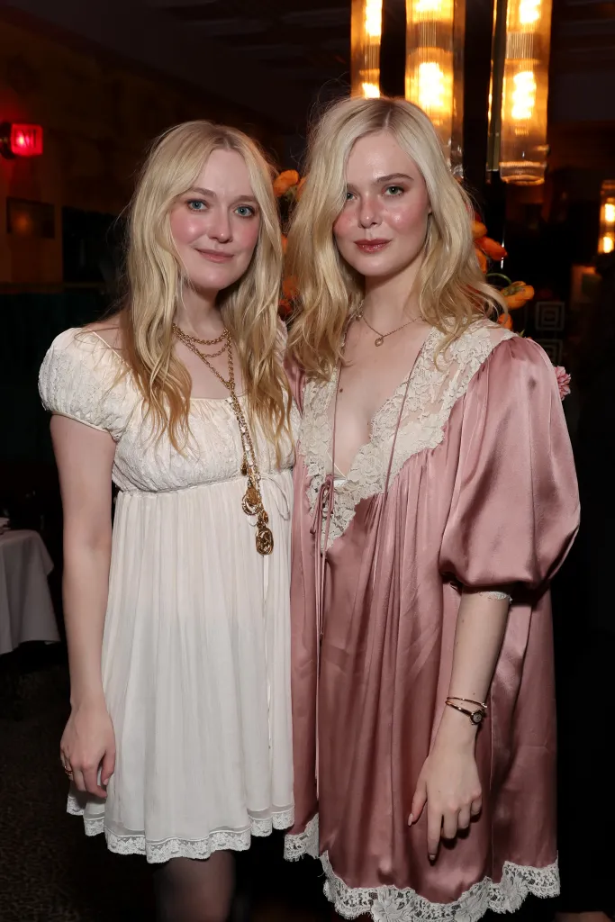 Dakota Fanning in a white lace dress and Elle Fanning in a pink lace dress posing for a photo.