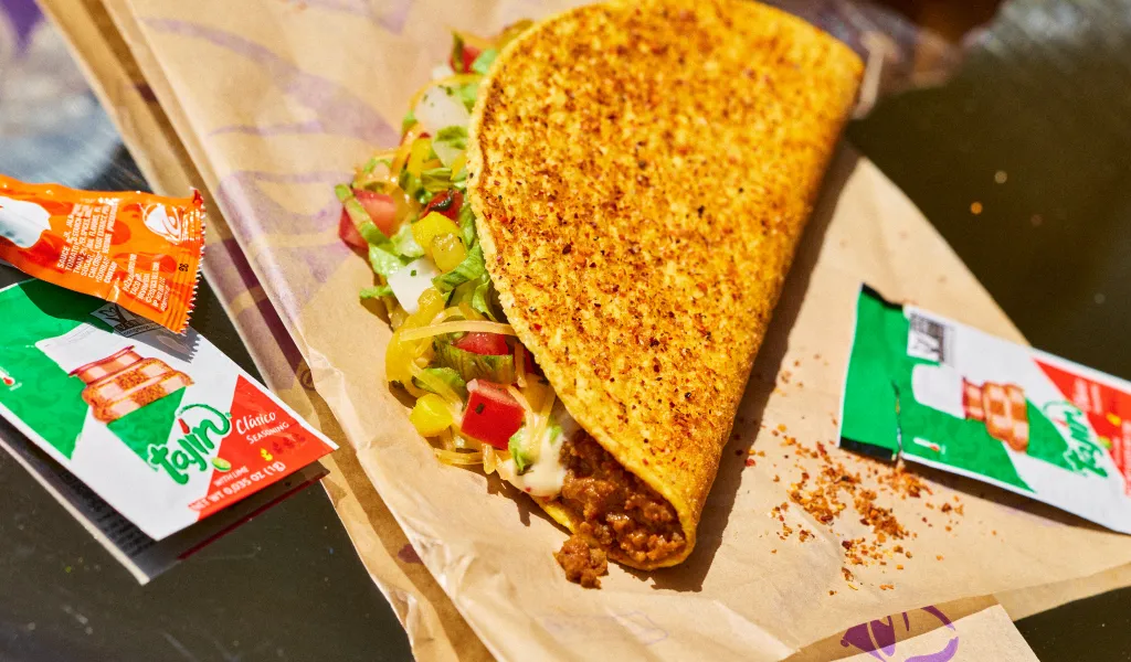 A taco from Taco Bell's Tajín lineup, served on parchment paper with packets of hot sauce and Tajín seasoning.