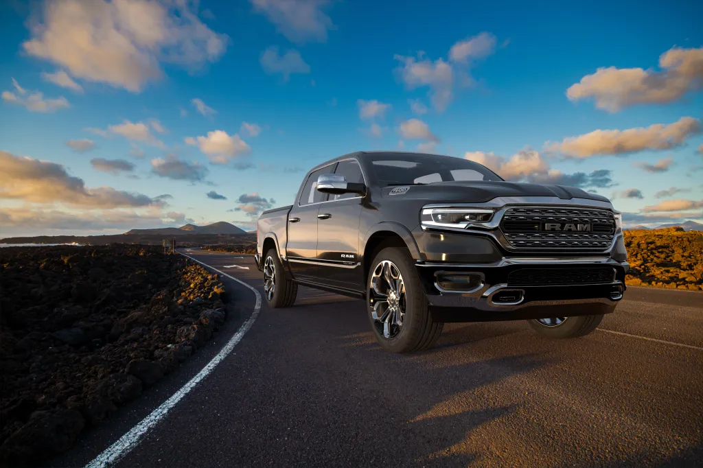 Black Dodge RAM 1500 truck on a road with volcanic rock fields under a blue and cloudy sky.