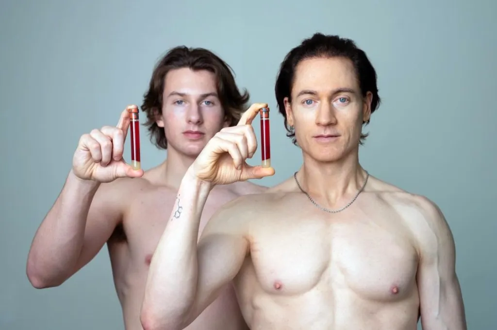 Bryan Johnson and a young man holding up vials of blood, shirtless, looking at the camera.