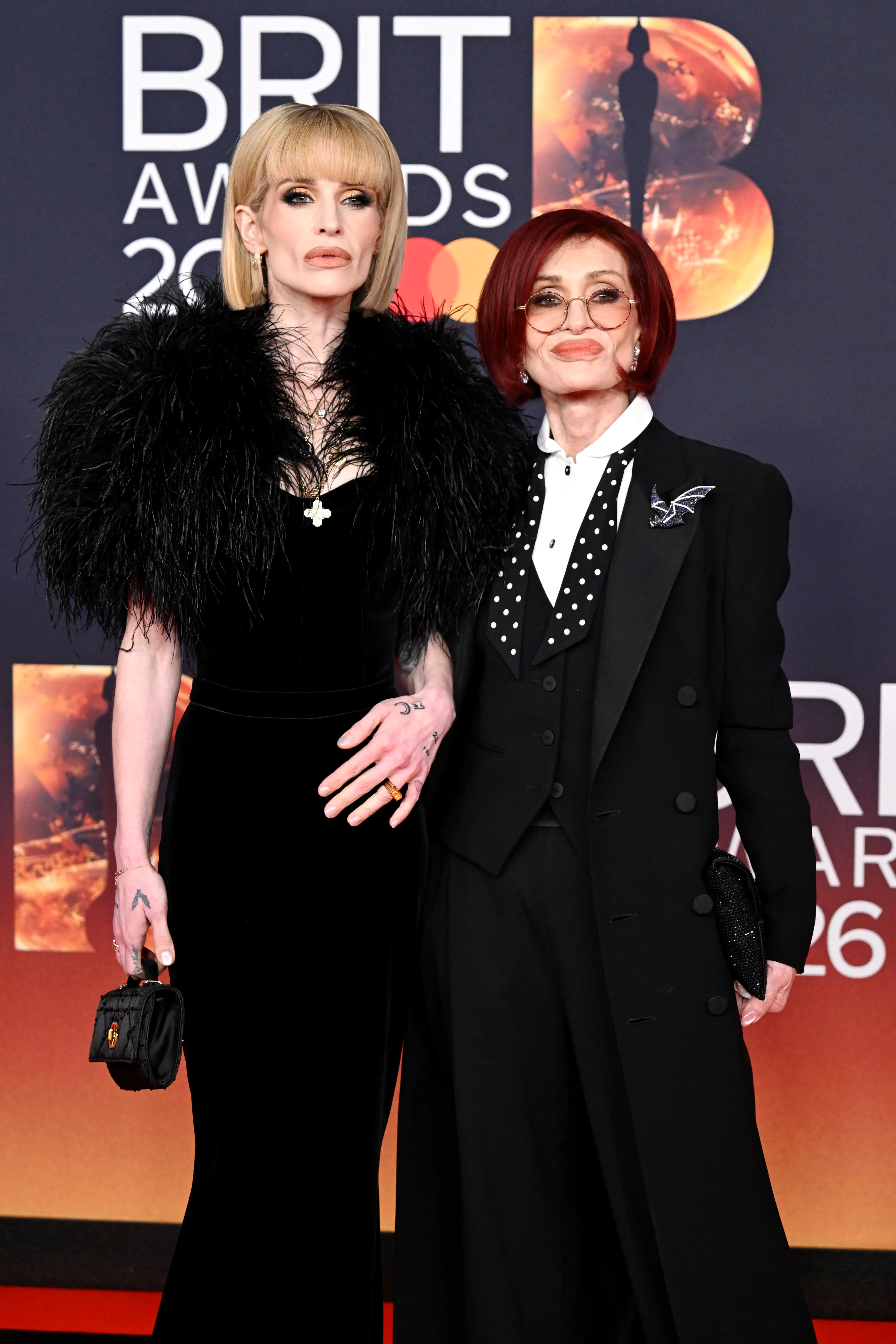Kelly Osbourne in a black feathered gown and Sharon Osbourne in a black suit.