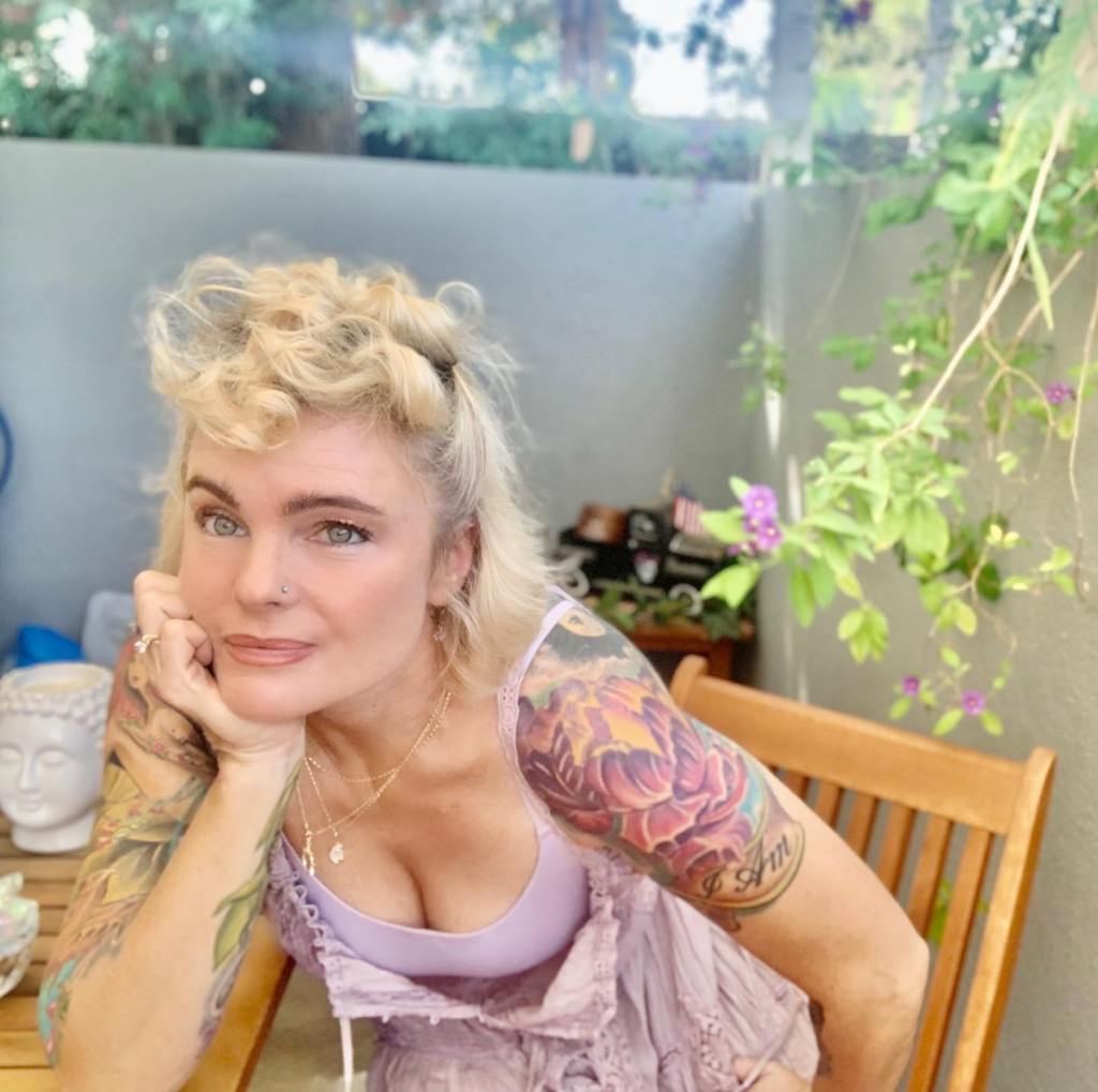 Erika Eleniak posing with a hand on her chin, showing off her shoulder tattoo.