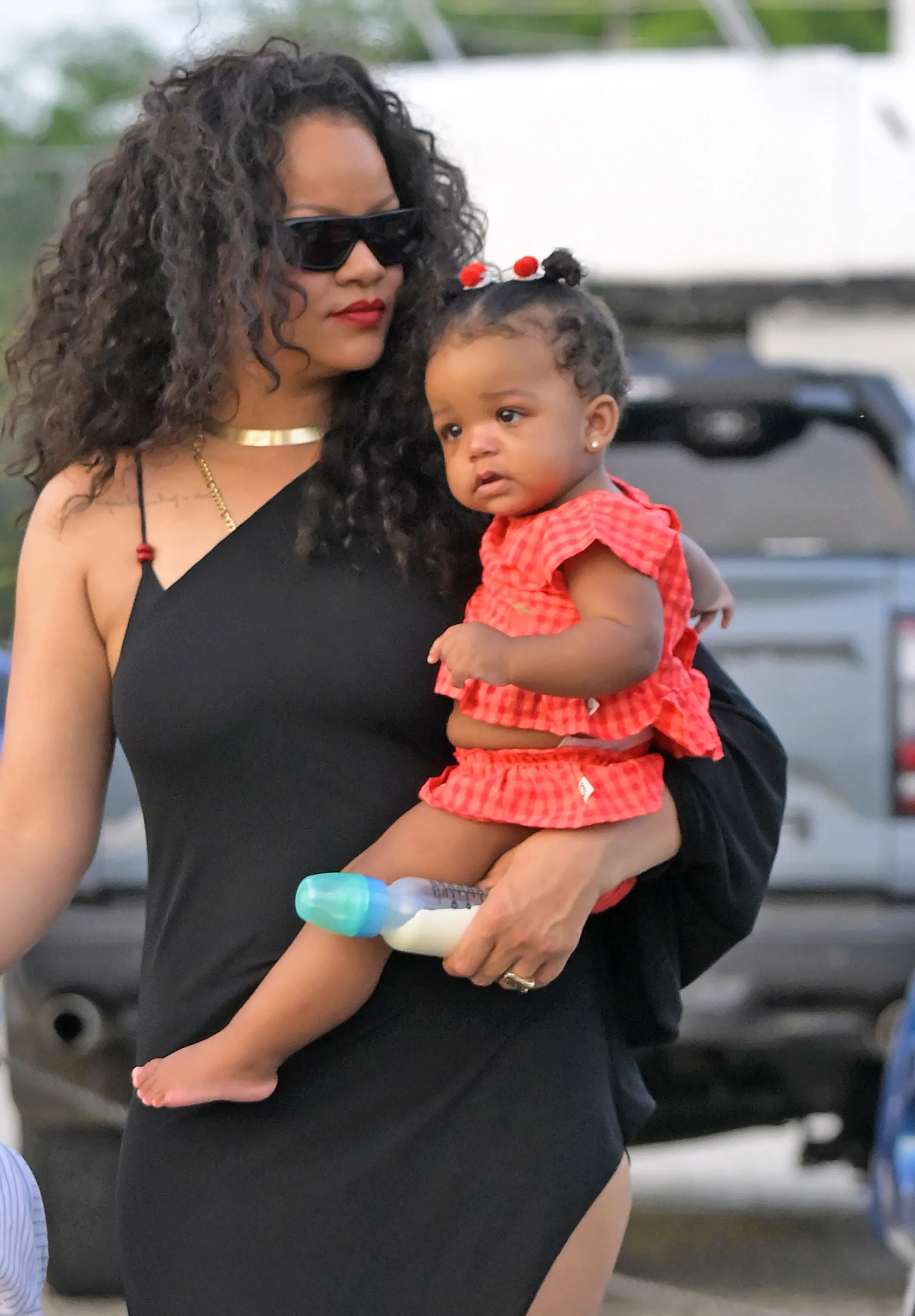 Rihanna holding her baby daughter Rocki, who holds a baby bottle, while on a family day out in Barbados.