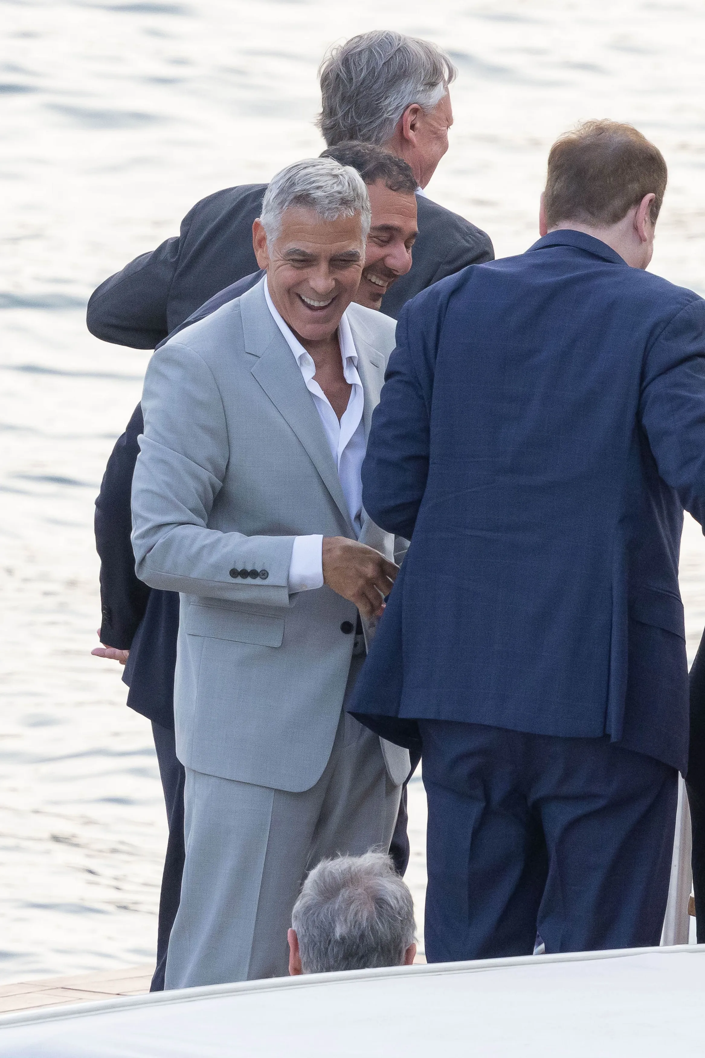 George Clooney, smiling, in a light gray suit, arrives at the Clooney Foundation For Justice fundraiser.