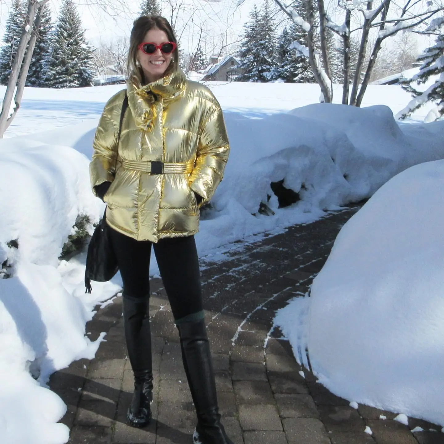 Maria Shriver in a gold puffer coat, black pants, and boots, standing on a snowy path.
