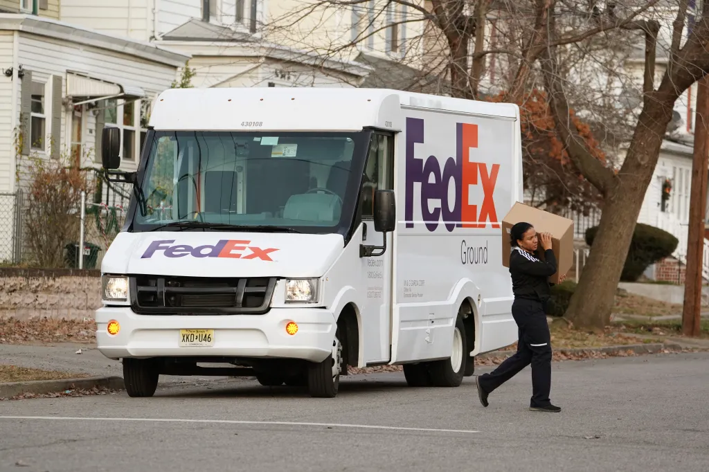 A FedEx delivery person carrying a package walks next to a FedEx delivery truck.