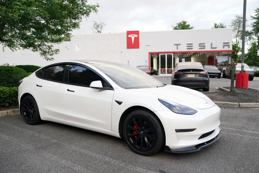 A white Tesla car parked in front of a Tesla car dealership.