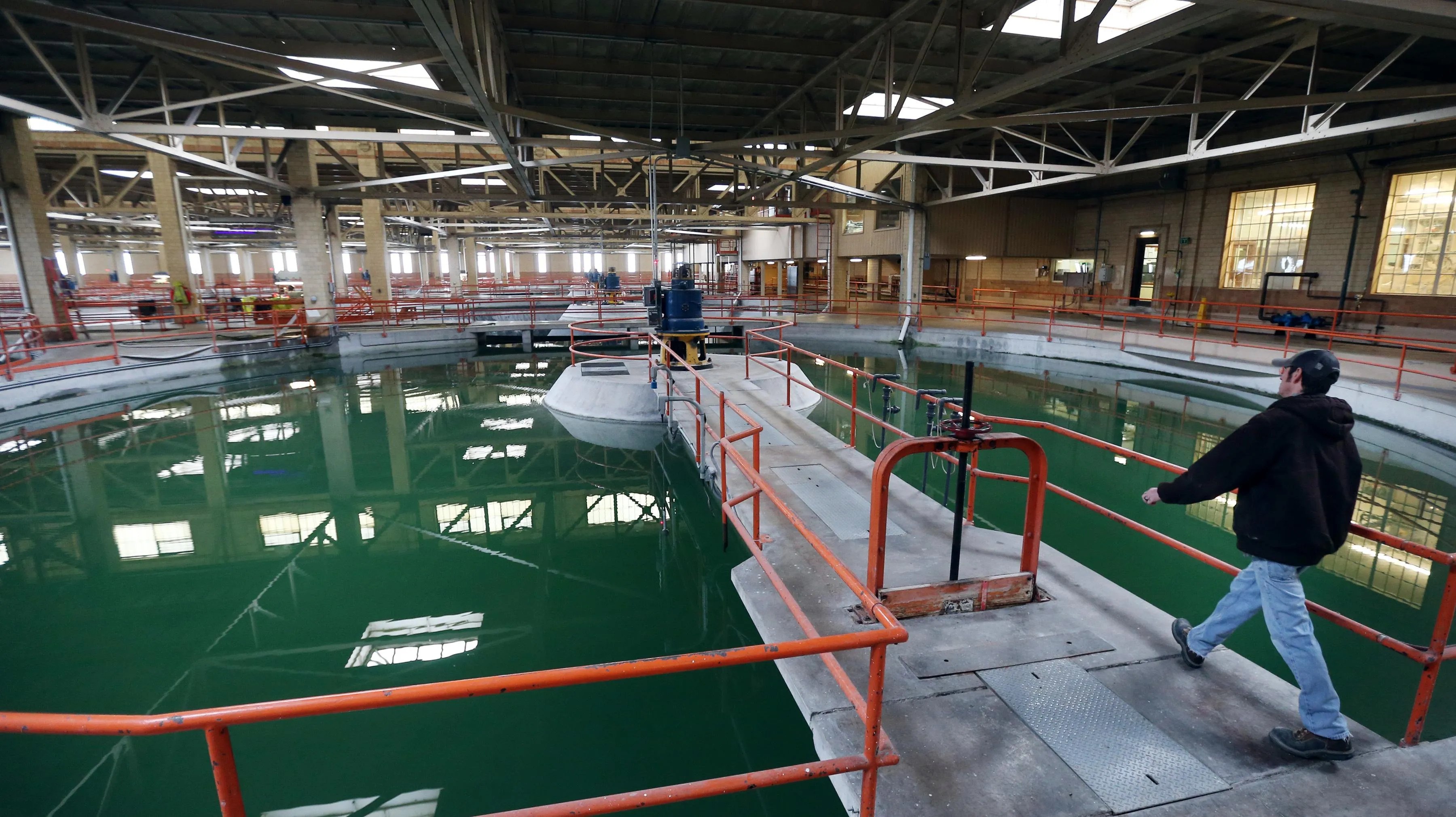 Workers on walkways over green lagoons in an indoor water treatment plant. Workers on walkways over green lagoons in an indoor water treatment plant.